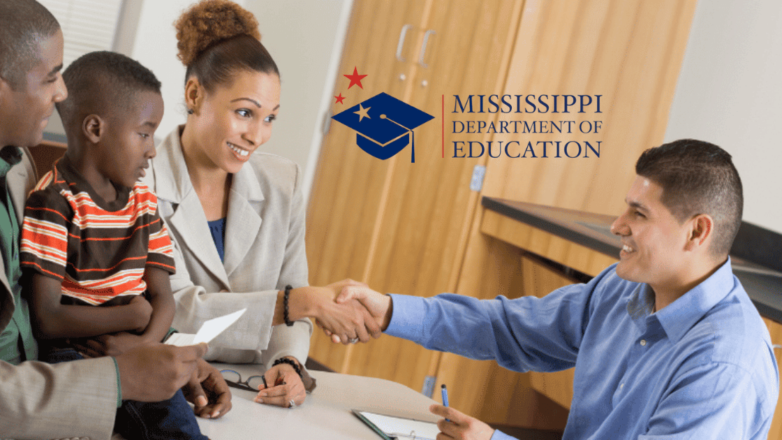 A man in a blue shirt shakes hands with a woman in a gray blazer while a man and a young boy sit beside her. The Mississippi Department of Education logo and the LA GATOR SCHOLARSHIP PROGRAM are visible on the wall.