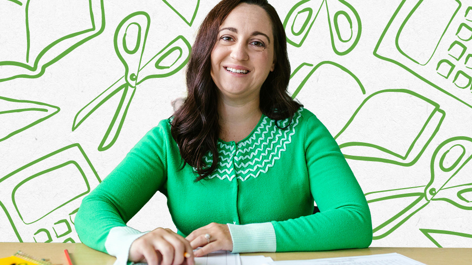 Teacher wearing a green sweater sitting at desk smiling